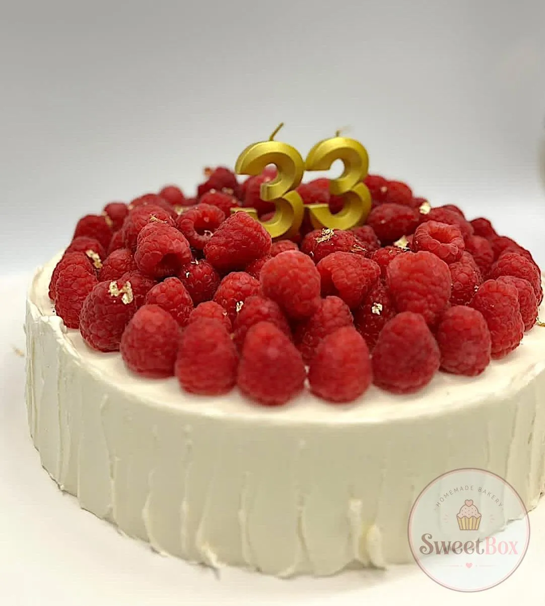 White cake covered with fresh raspberries and a gold number 33 candle