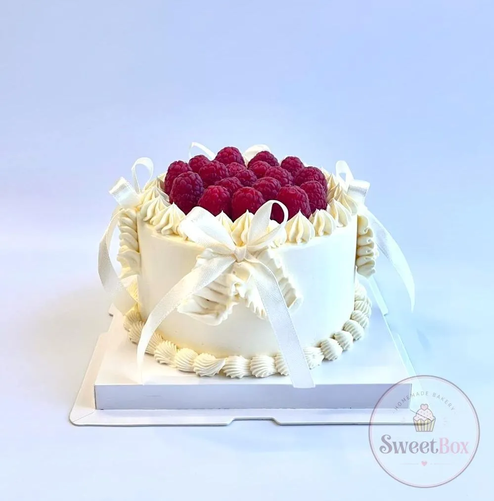 White vintage-style cake topped with fresh raspberries and wrapped with cream satin bows
