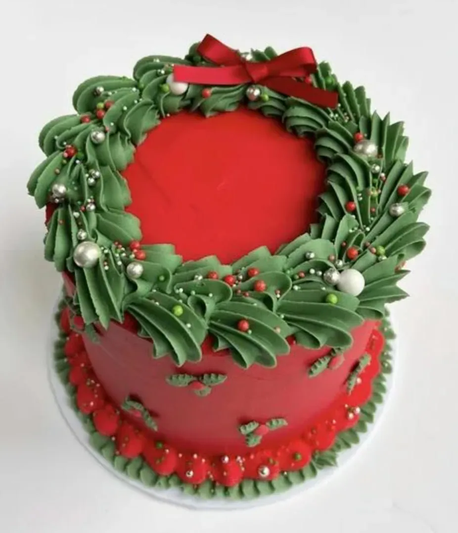 Example of a Christmas wreath design: a red cake with a piped green wreath, a red satin bow and silver and red sugar pearls