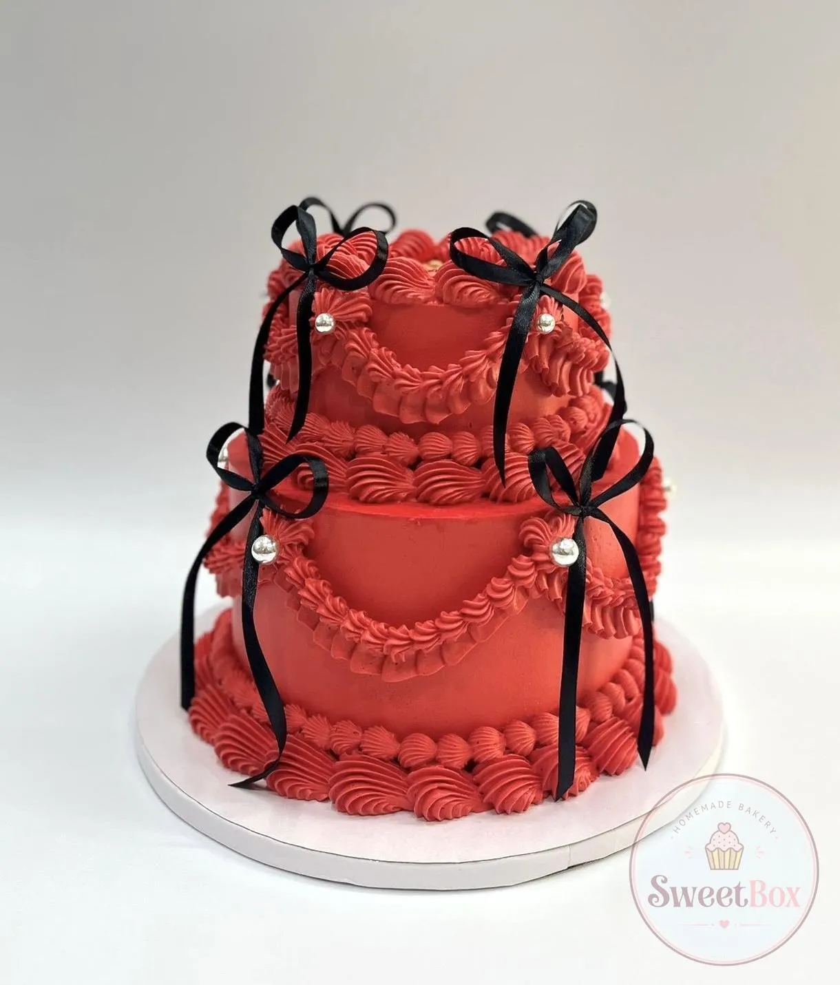Two-tier red vintage cake with piped swags, silver pearls and black ribbon bows