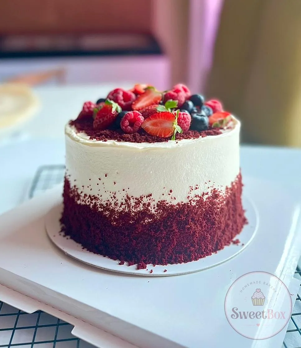 Semi-naked red velvet cake with white cream and a topping of strawberries, raspberries and blueberries
