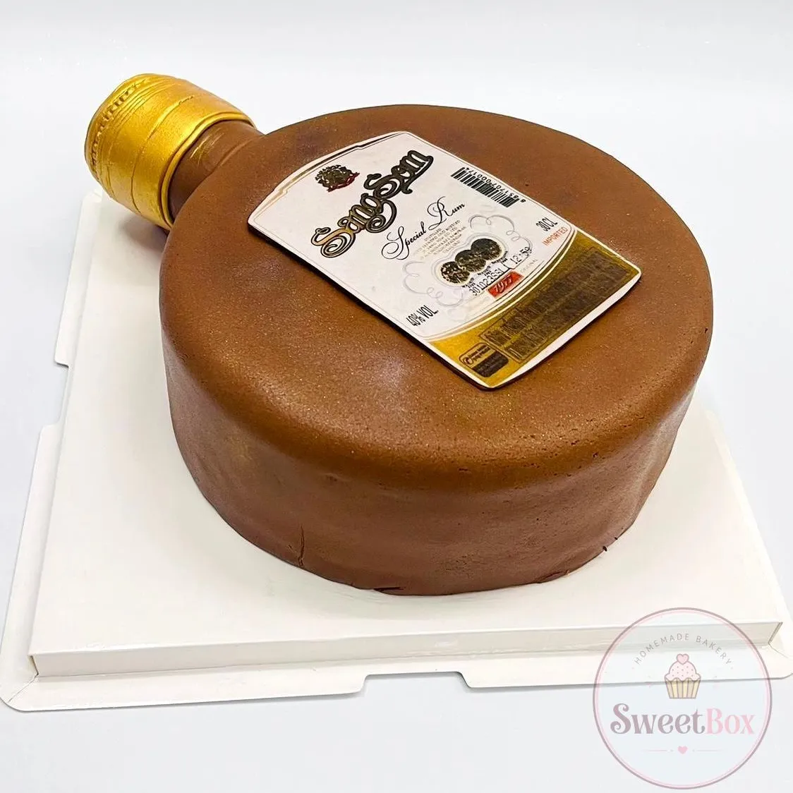 Cake shaped like a flat round rum bottle with a gold cap and printed label