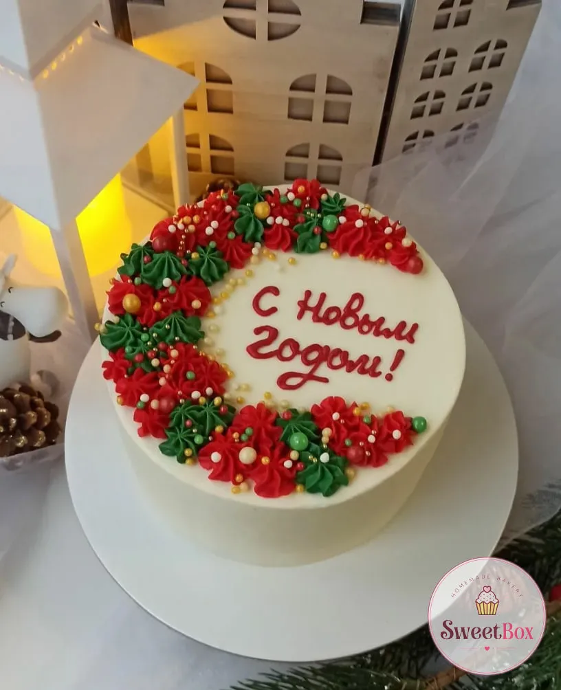 White cake with a crescent of red and green cream rosettes, gold pearls and a red Happy New Year greeting written in Russian
