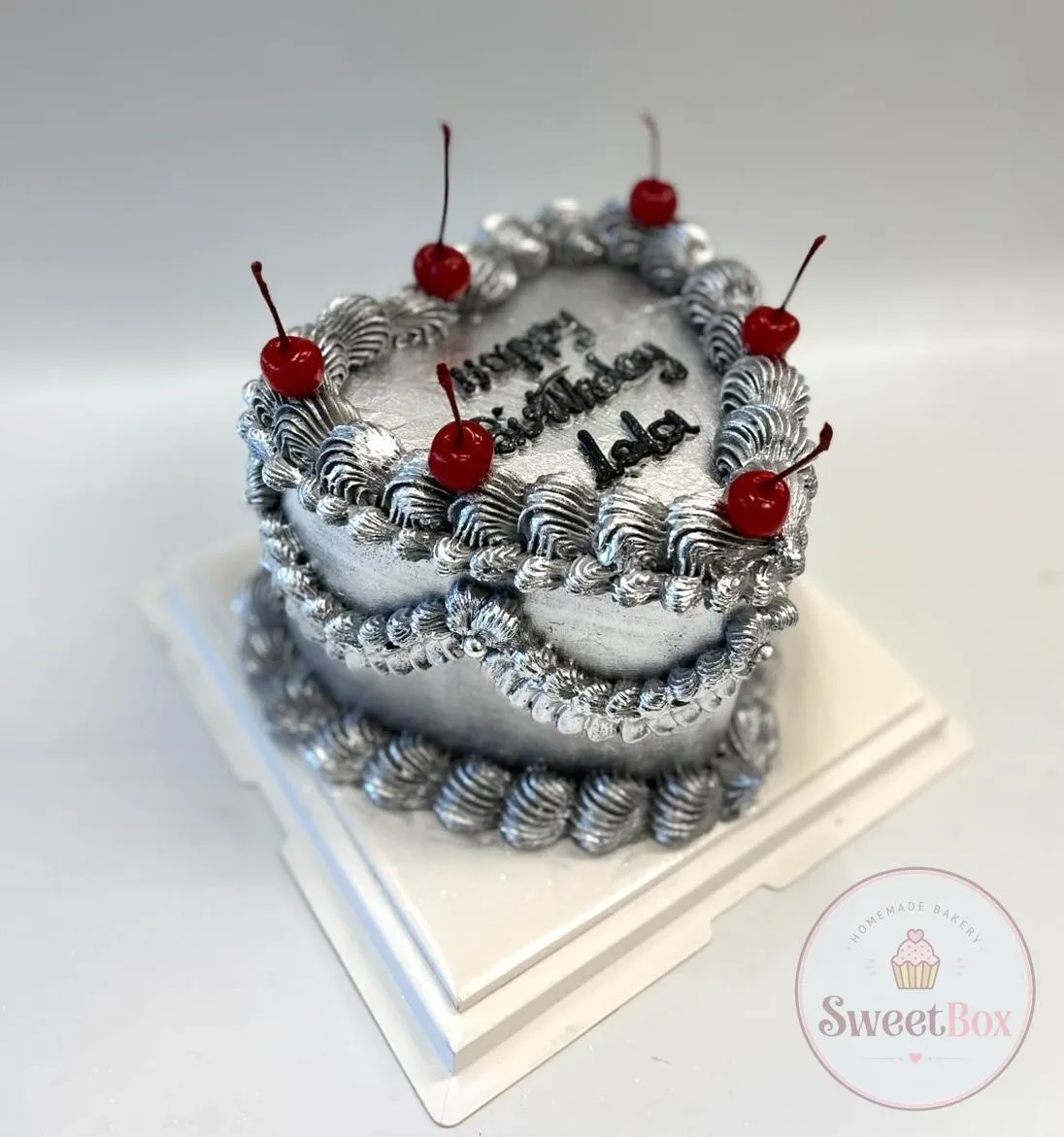Silver heart-shaped vintage cake with shiny piping, red cherries and a Happy Birthday message