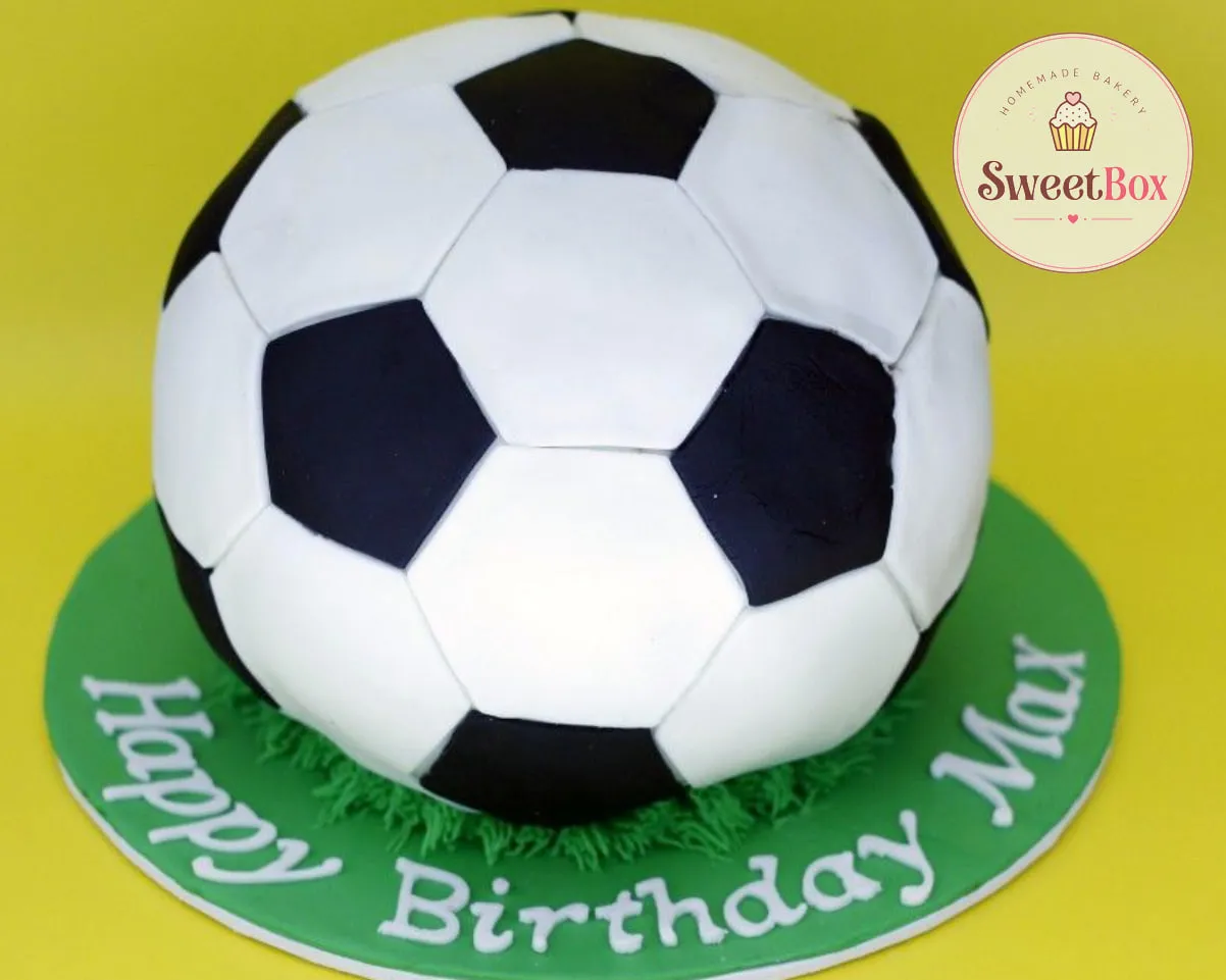 Whole soccer ball cake in black and white fondant on piped grass and a green board with Happy Birthday Max lettering