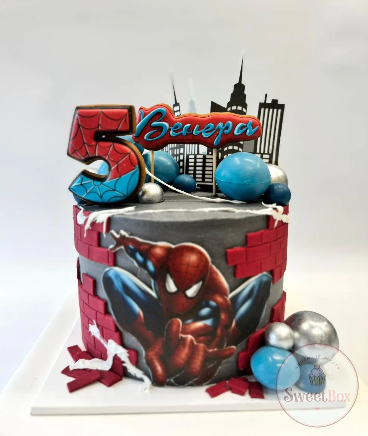 Gray Spider-Man cake with city skyline topper, brick wall details and a red and blue number 5