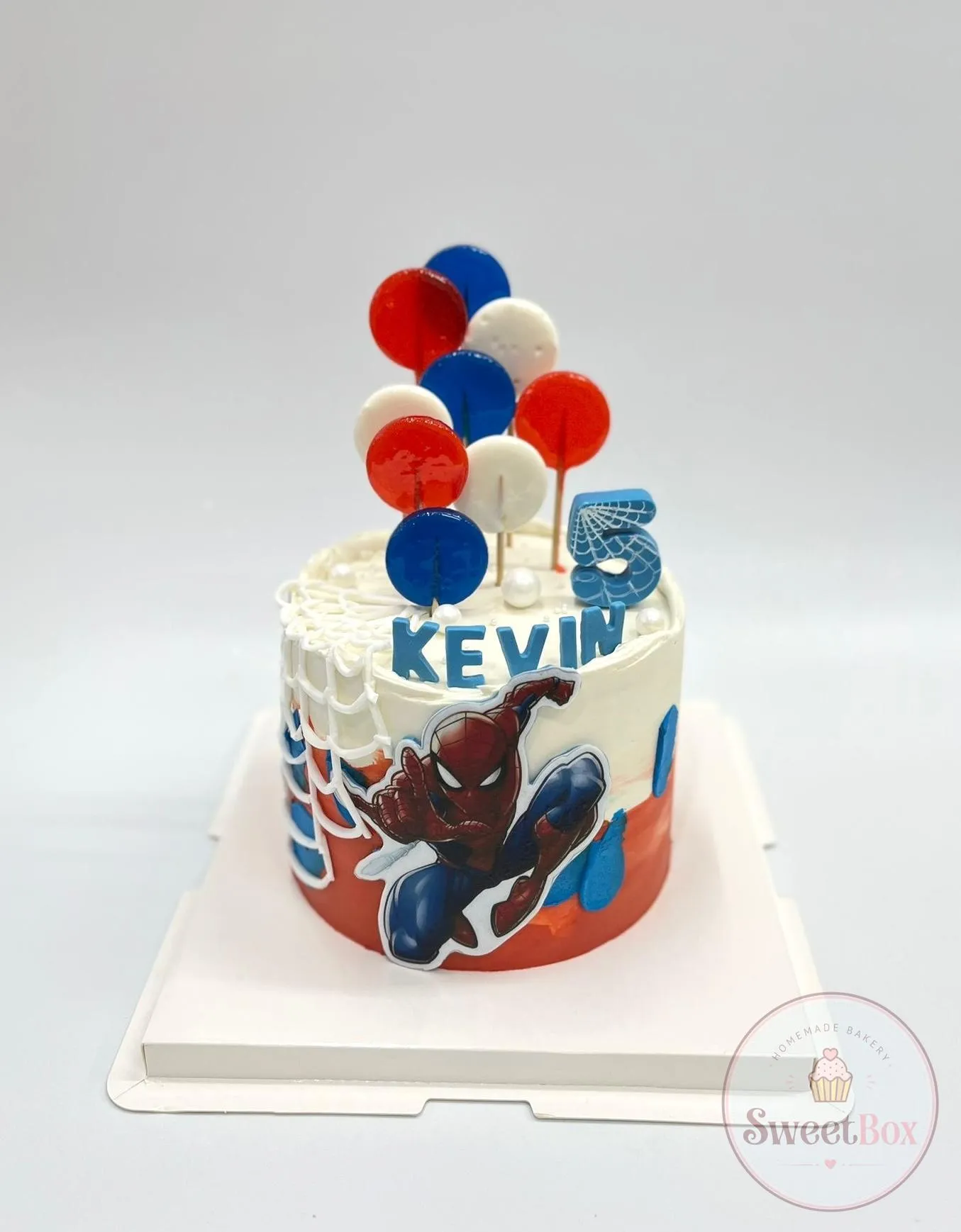 White and red cake with a Spider-Man picture, piped web, red, blue and white lollipops and a name with a 5