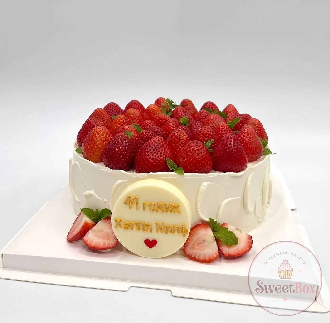Round white cake topped with fresh strawberries and a round personalized greeting plaque