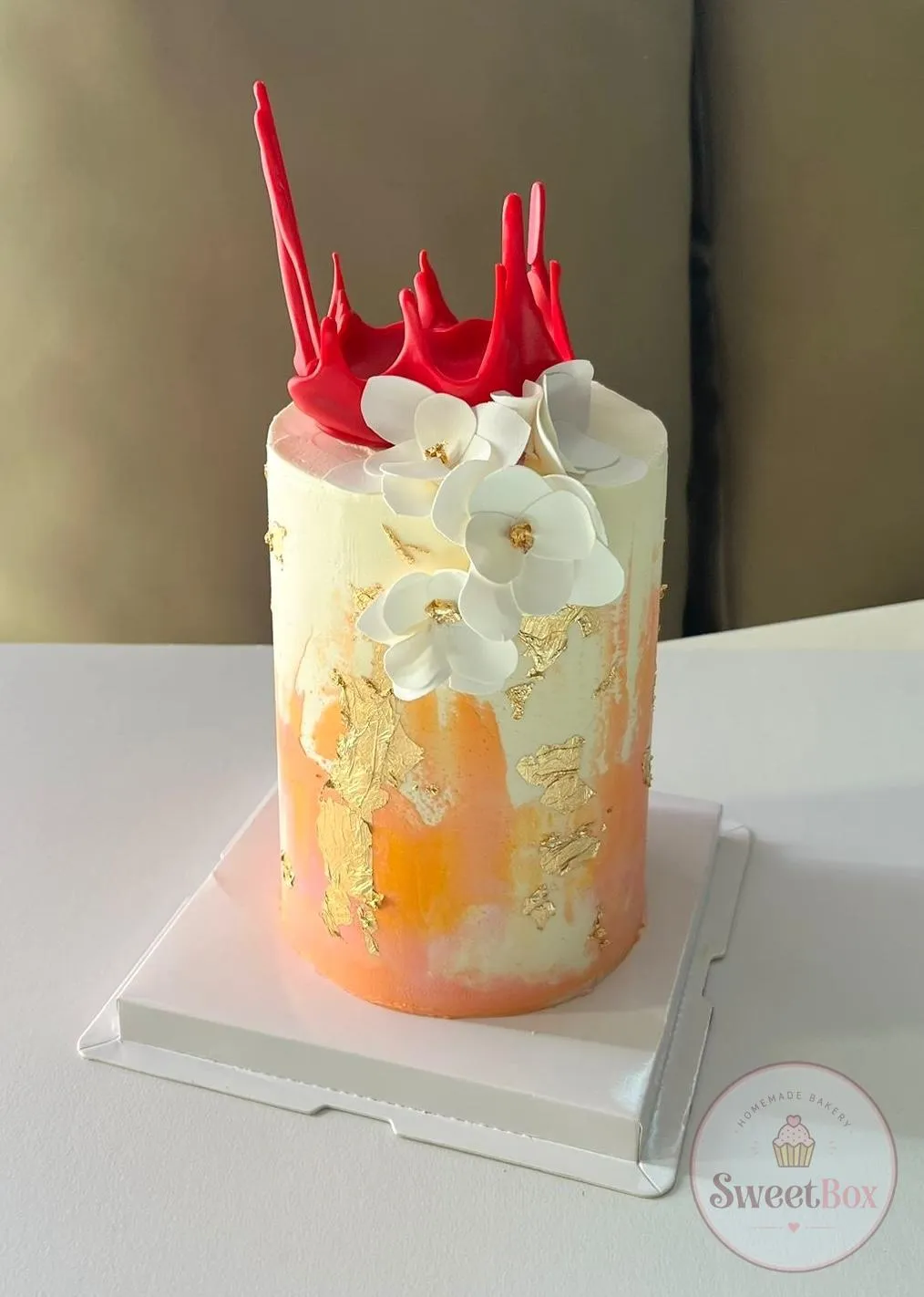 Tall peach and white cake with red chocolate sails, white sugar flowers and gold leaf