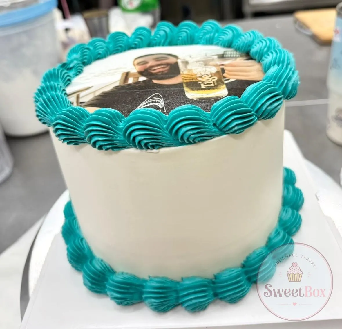 Tall white cake with teal piped borders and an edible photo print on top