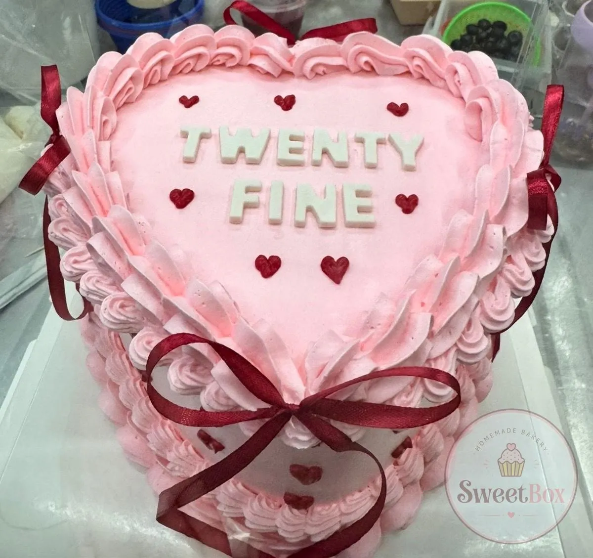 Pale pink heart cake with ruffled piping, small red hearts, burgundy ribbon bows and Twenty Fine lettering