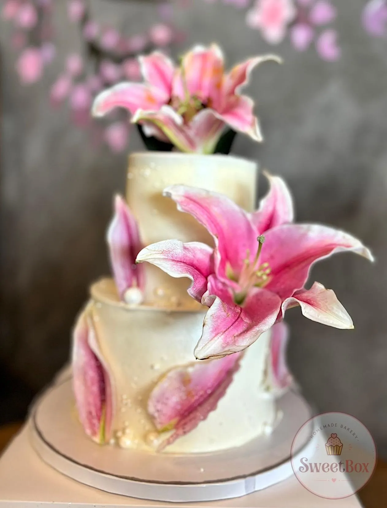 Two-tier white cake decorated with large pink sugar lilies and pearls