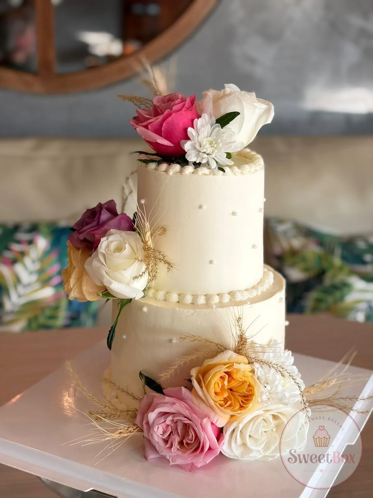 Two-tier ivory cake with pearl borders decorated with fresh pink, white and peach roses