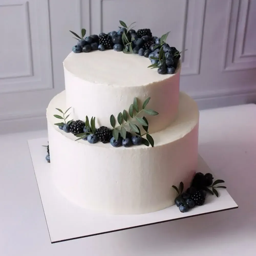 Two-tier white cake with blackberries, blueberries and olive leaves