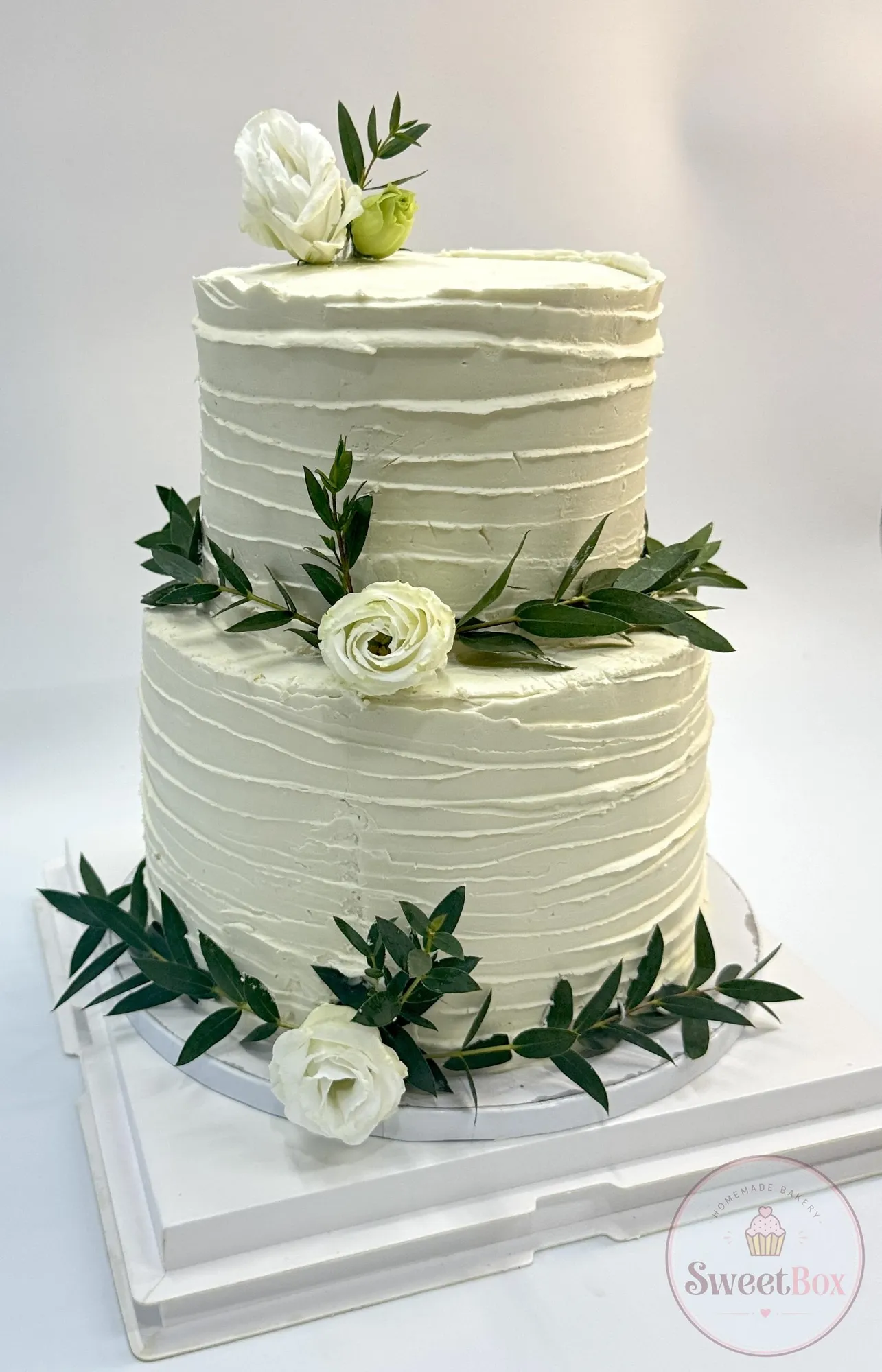 Two-tier textured white cake decorated with white flowers and fresh green leaves