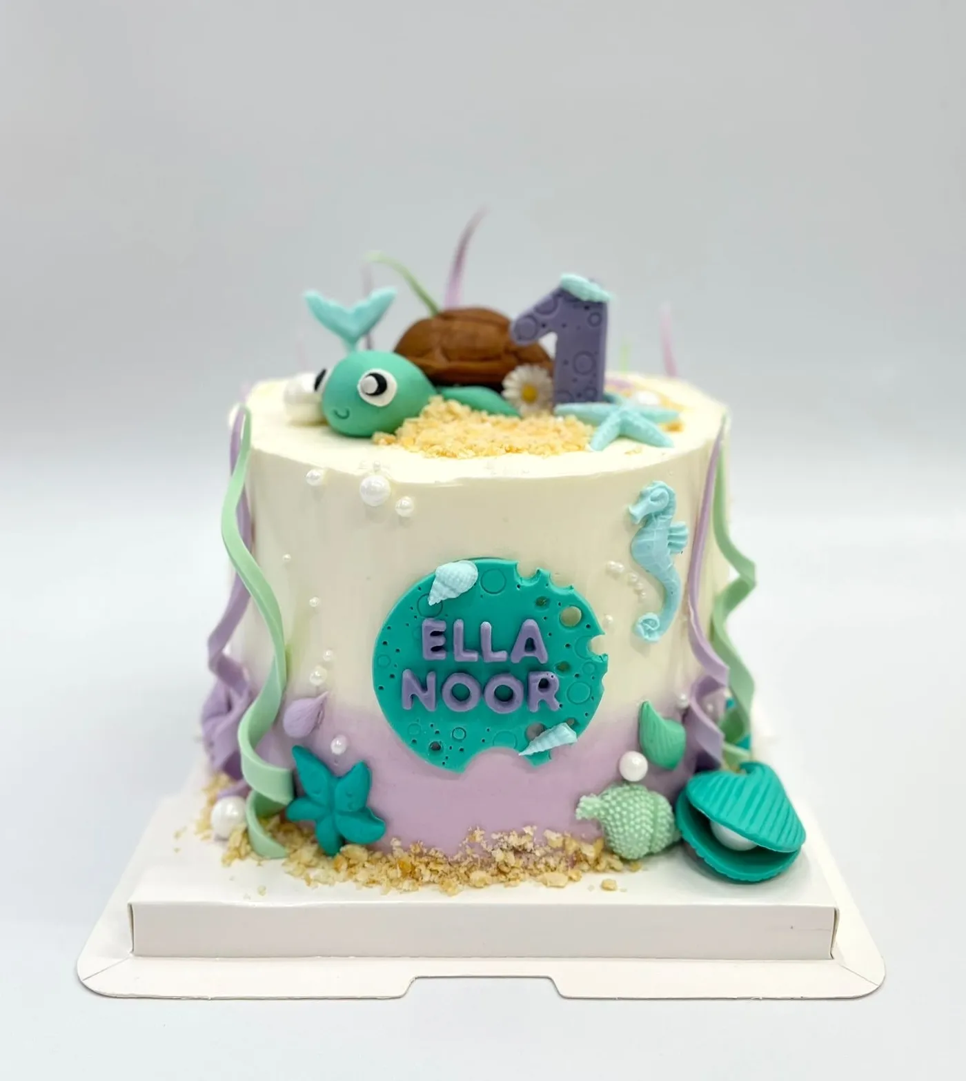 Under-the-sea first birthday cake with a sea turtle, number 1, seahorse, shells and a teal name plaque