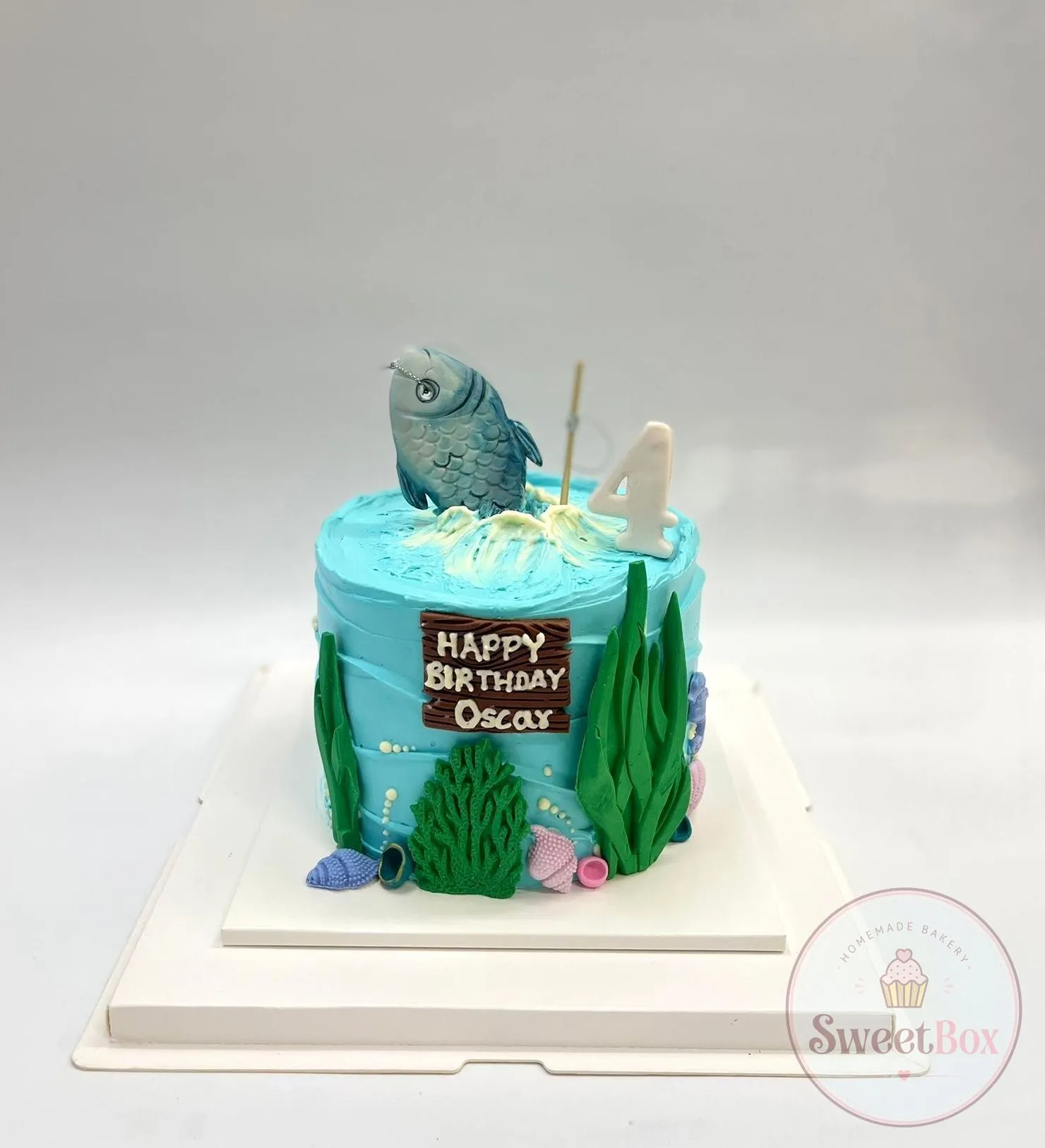 Blue ocean-themed birthday cake with a sugar fish, seaweed, shells and a Happy Birthday name plaque