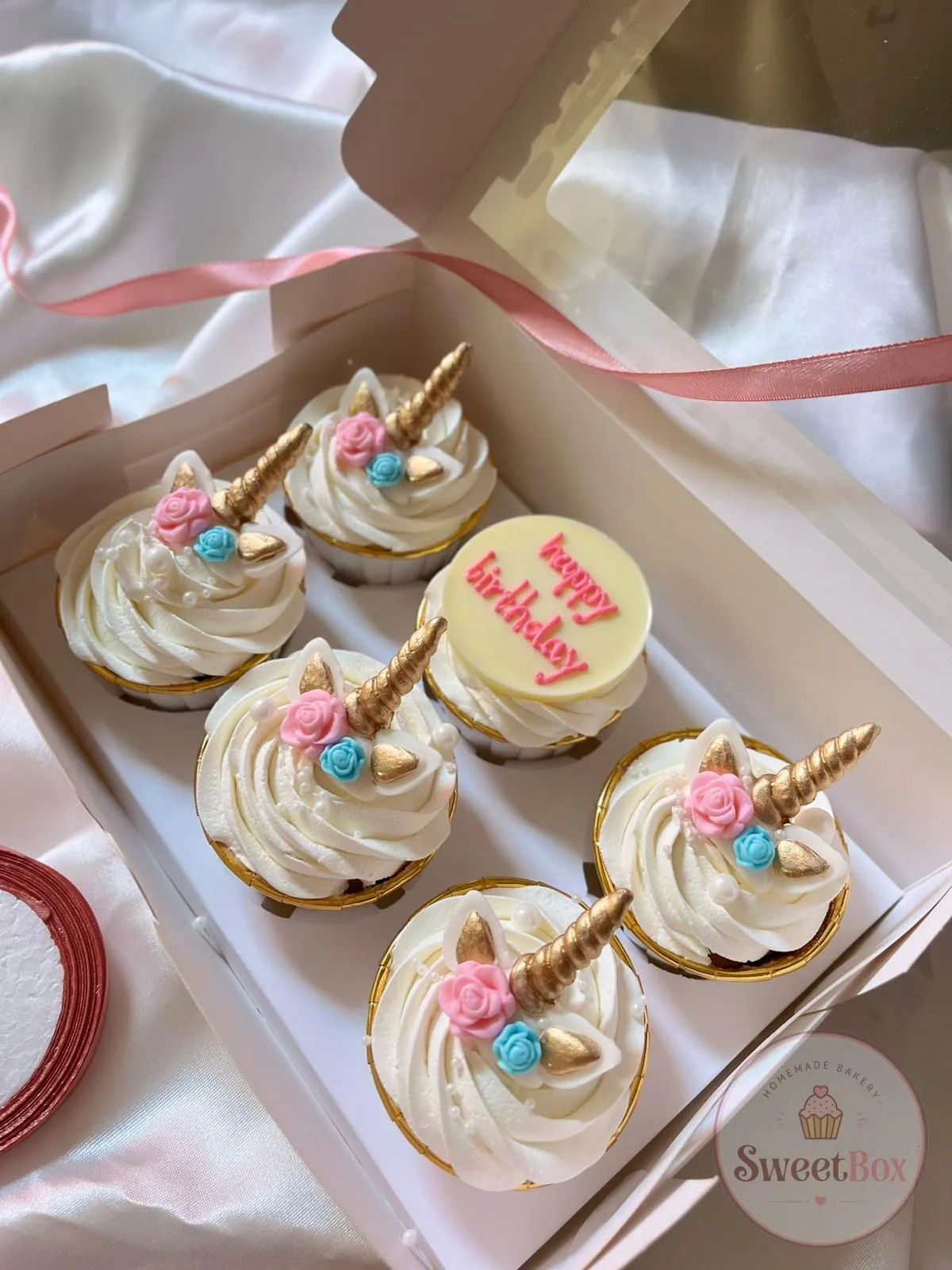 Box of cream cupcakes with gold unicorn horns and pink and blue roses, plus one with a Happy Birthday disc