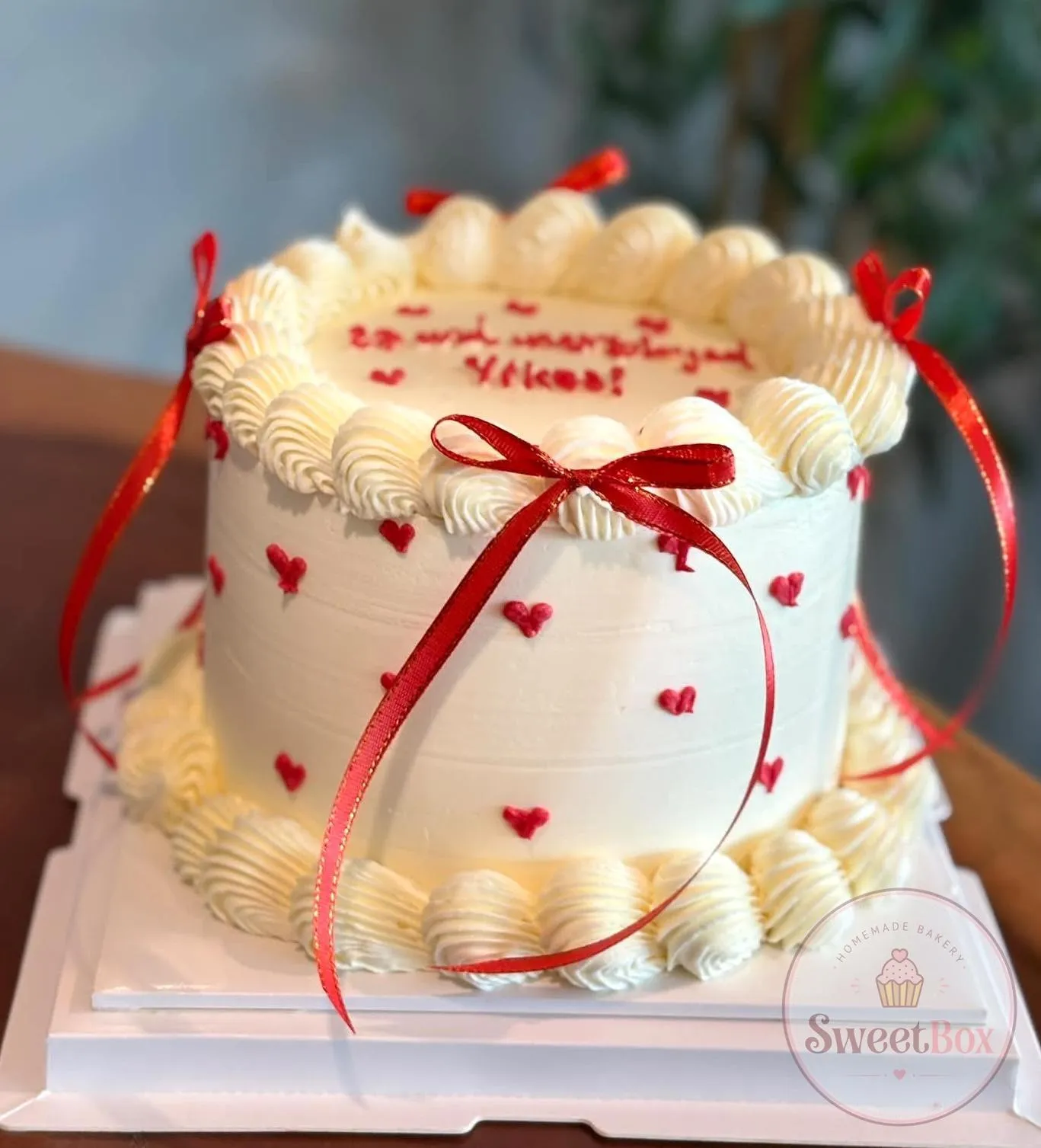 White vintage cake with cream shell piping, tiny red hearts and red satin ribbon bows