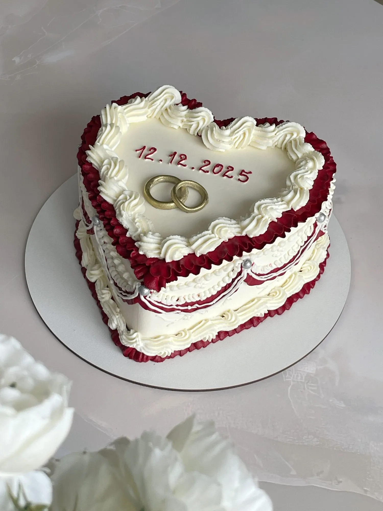 Heart-shaped vintage cake with burgundy ruffles, white piping, two gold rings and a date