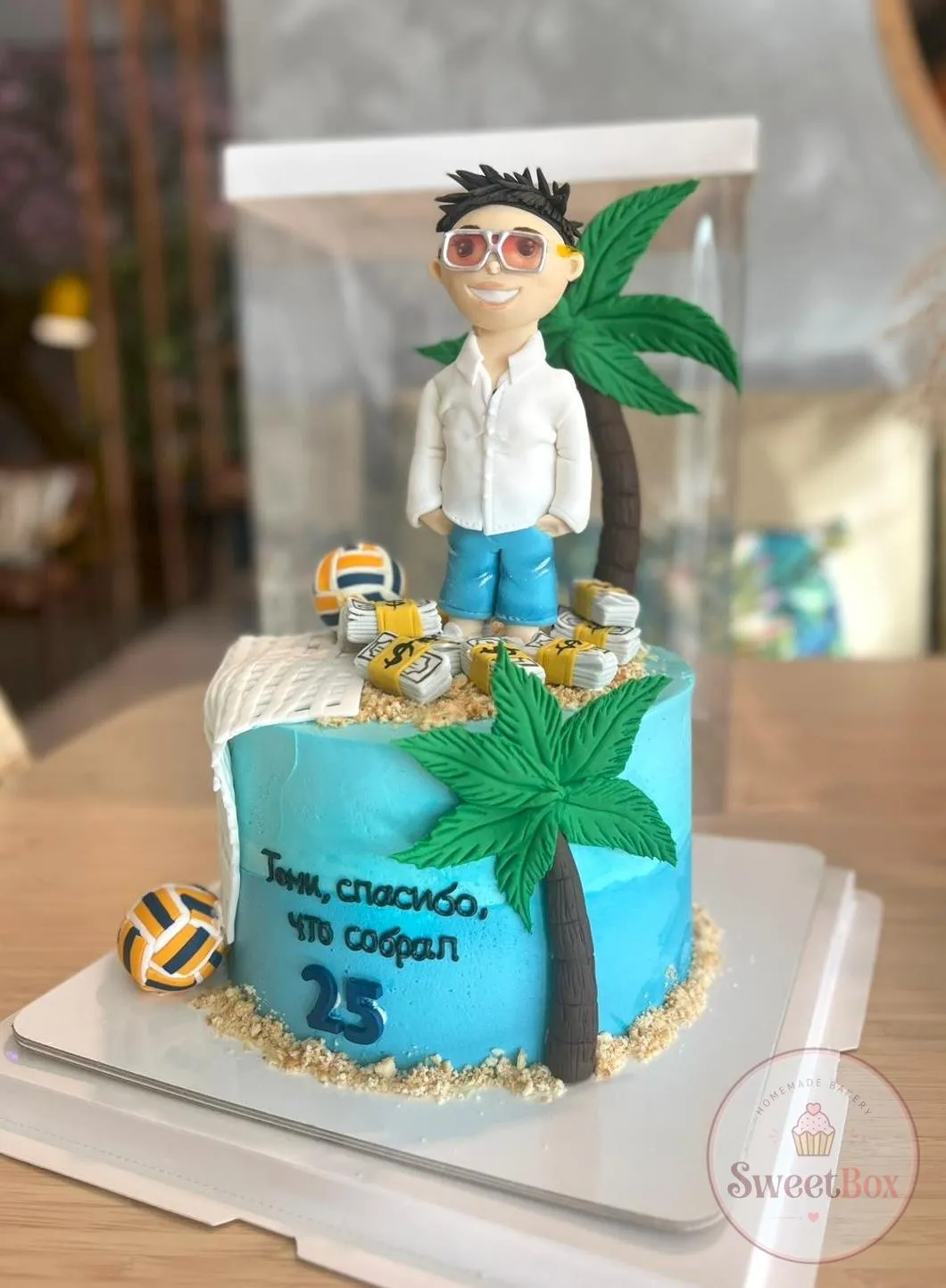 Blue beach-themed volleyball cake with a man figurine, fondant palm trees and volleyball decorations