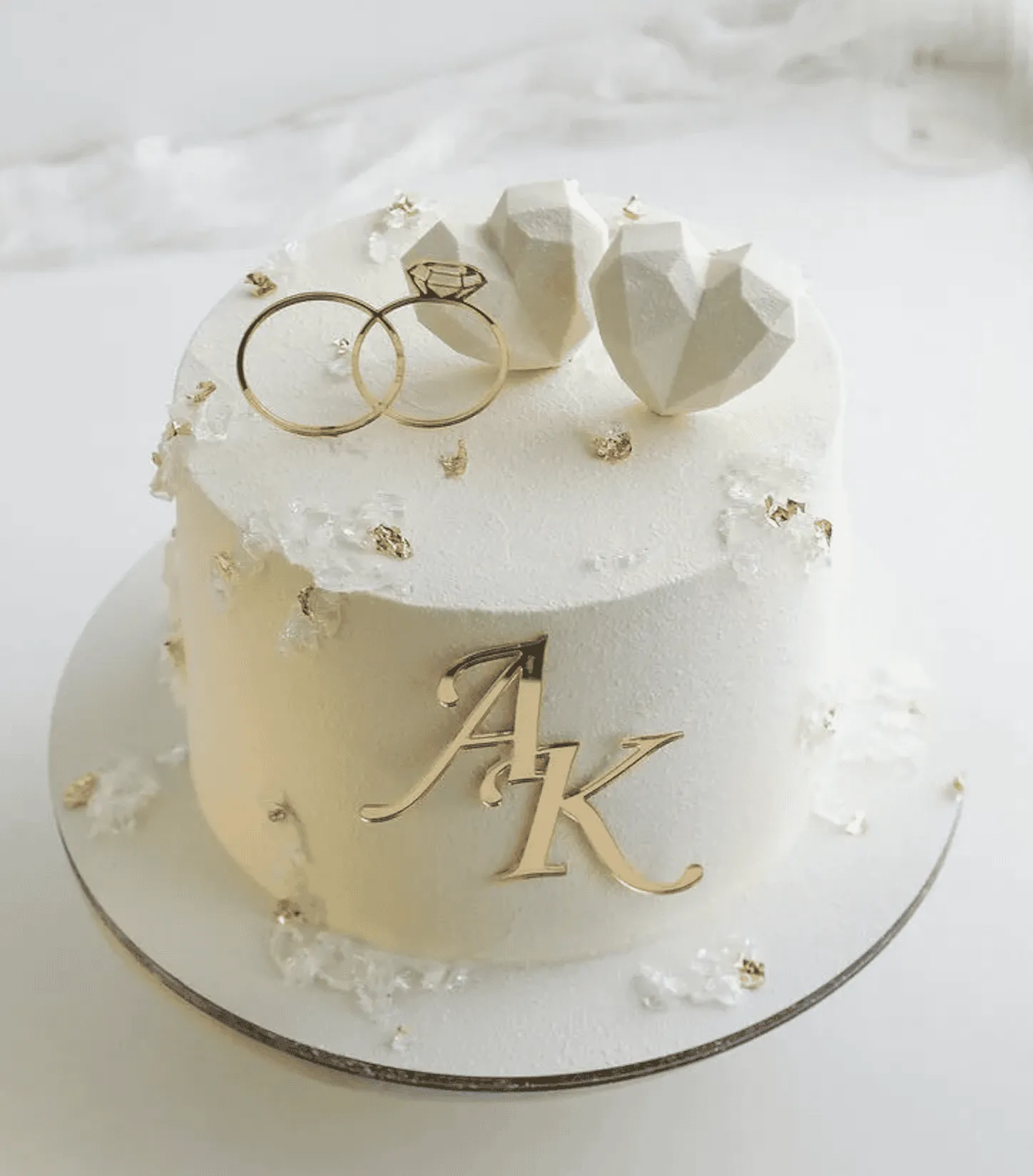 White cake with gold rings, geometric white hearts and a gold initials monogram