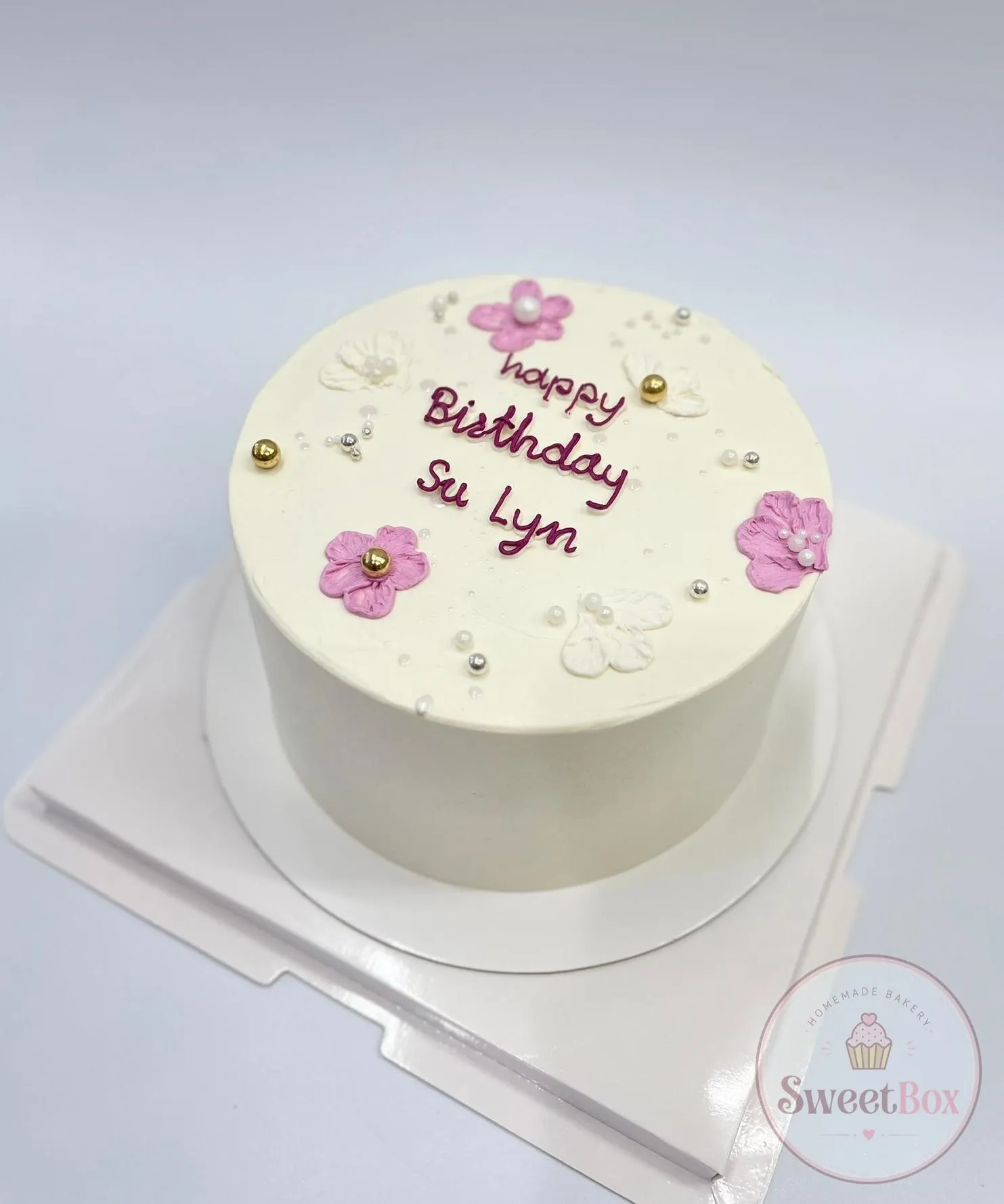 White bento cake with Happy Birthday script, pink sugar flowers and gold pearls, personalized with a name