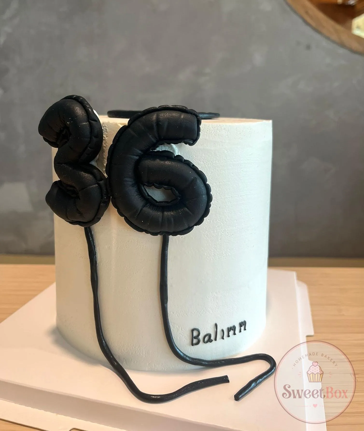Tall white cake with black number 36 balloon toppers and a name written on the side