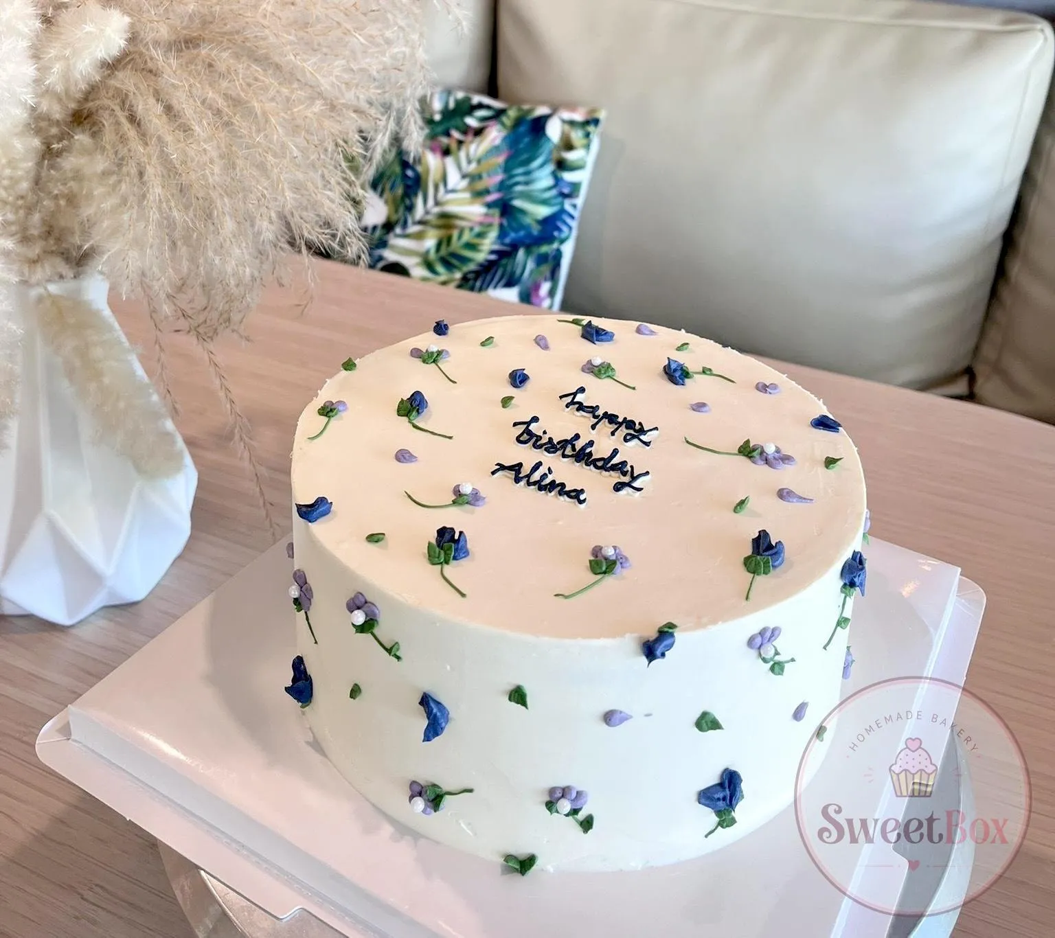 White cake scattered with tiny blue and purple piped flowers and a Happy Birthday message