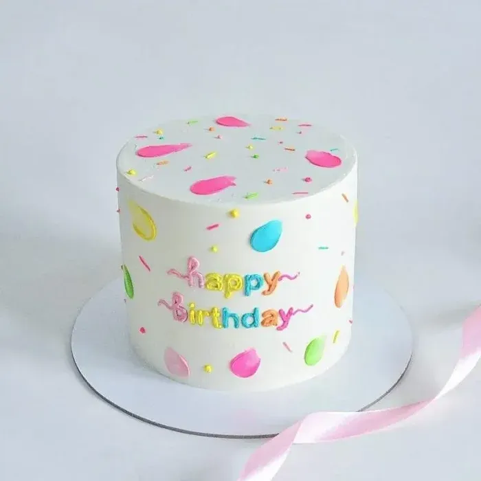 White minimalist cake with neon balloon shapes, sprinkles and rainbow Happy Birthday lettering