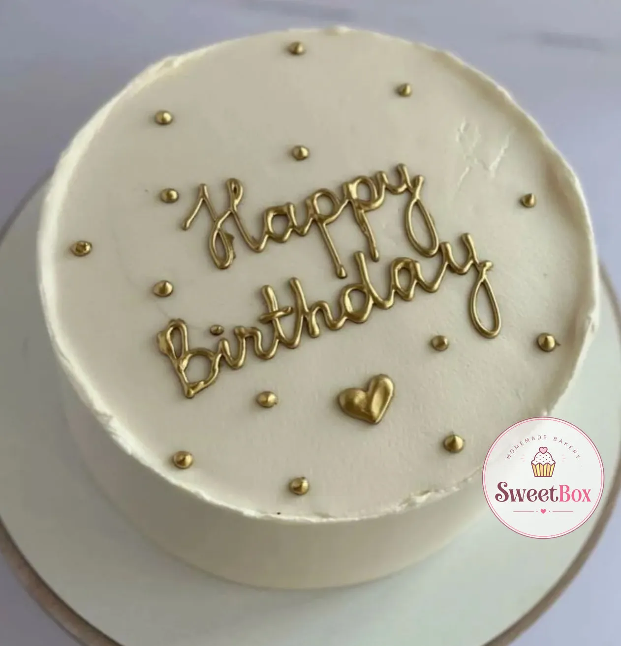 Ivory cake with gold Happy Birthday script, a small gold heart and gold dots on top