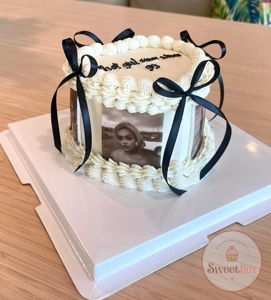 White cake with a black and white portrait print around the side, piped borders and black ribbon bows