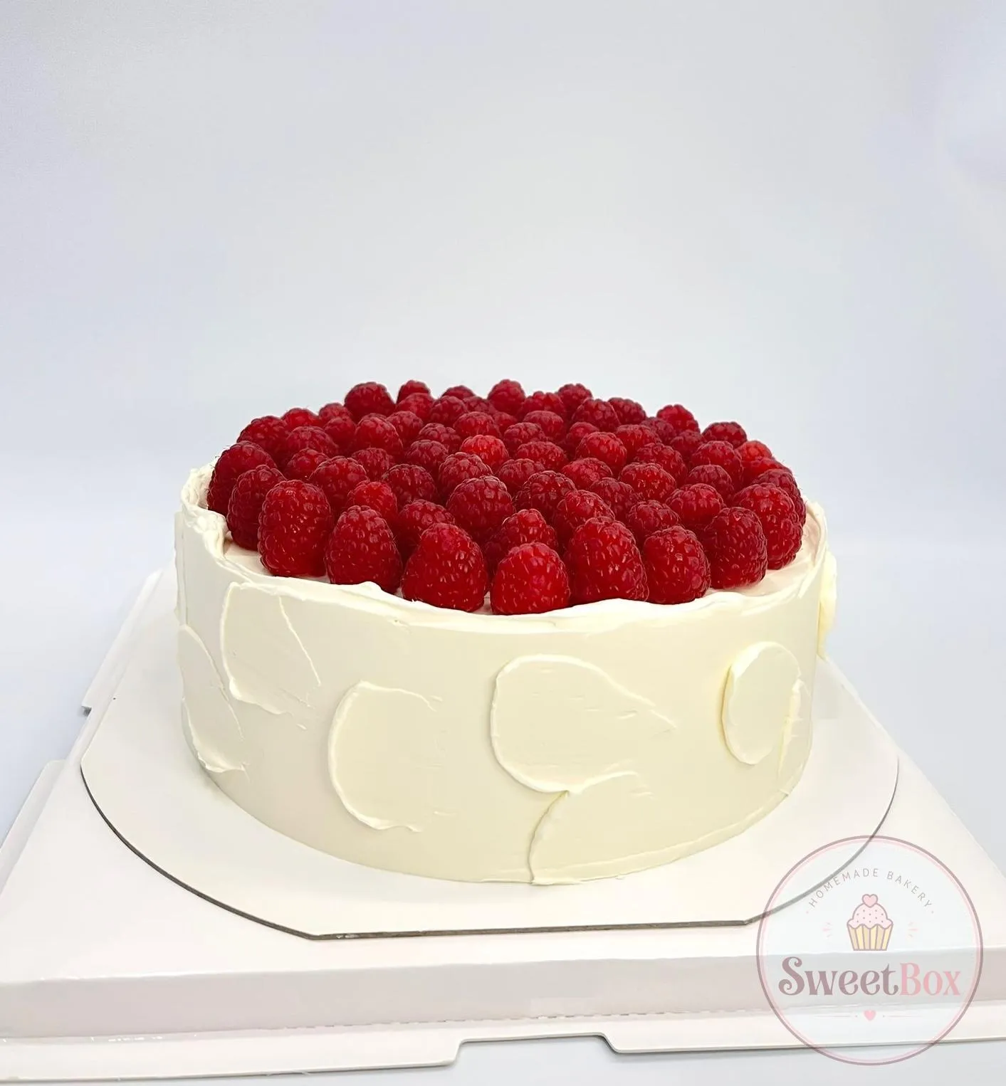 White cake with swirled buttercream texture, topped with a layer of fresh raspberries