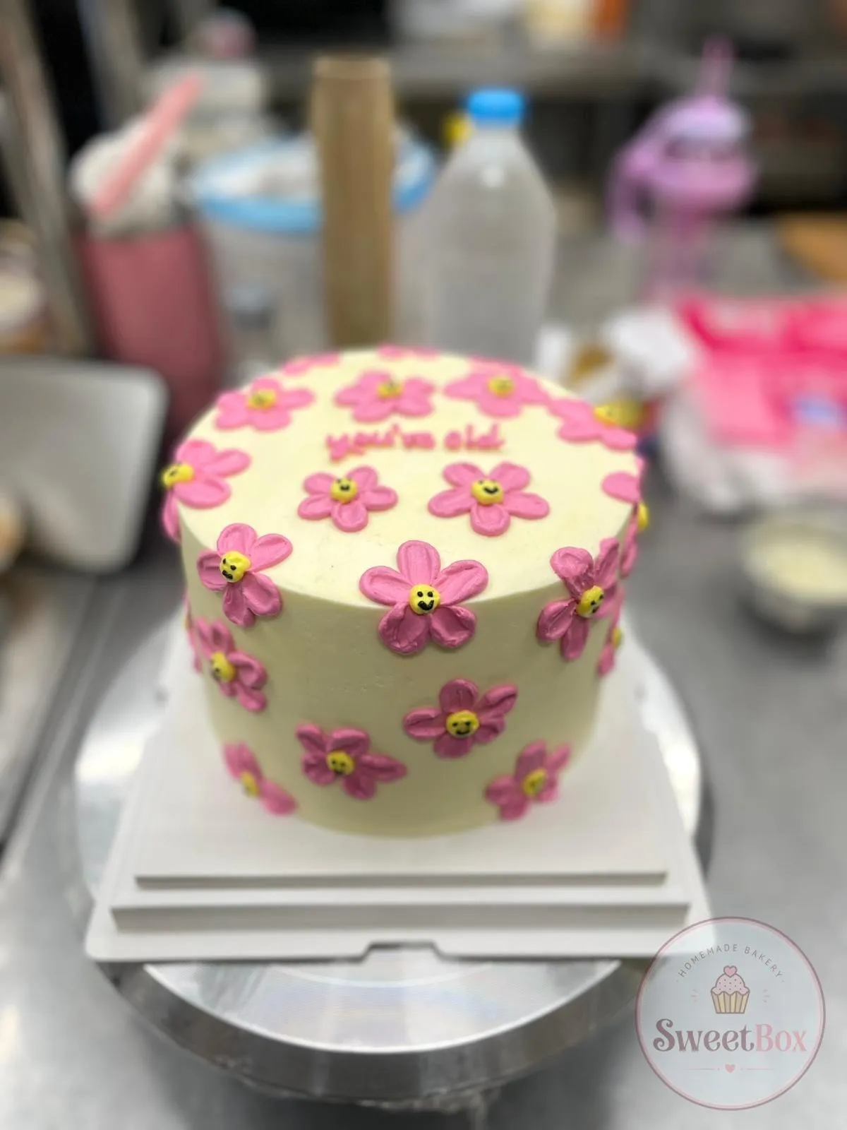 Pale yellow bento cake covered in piped pink daisies with smiling yellow centers