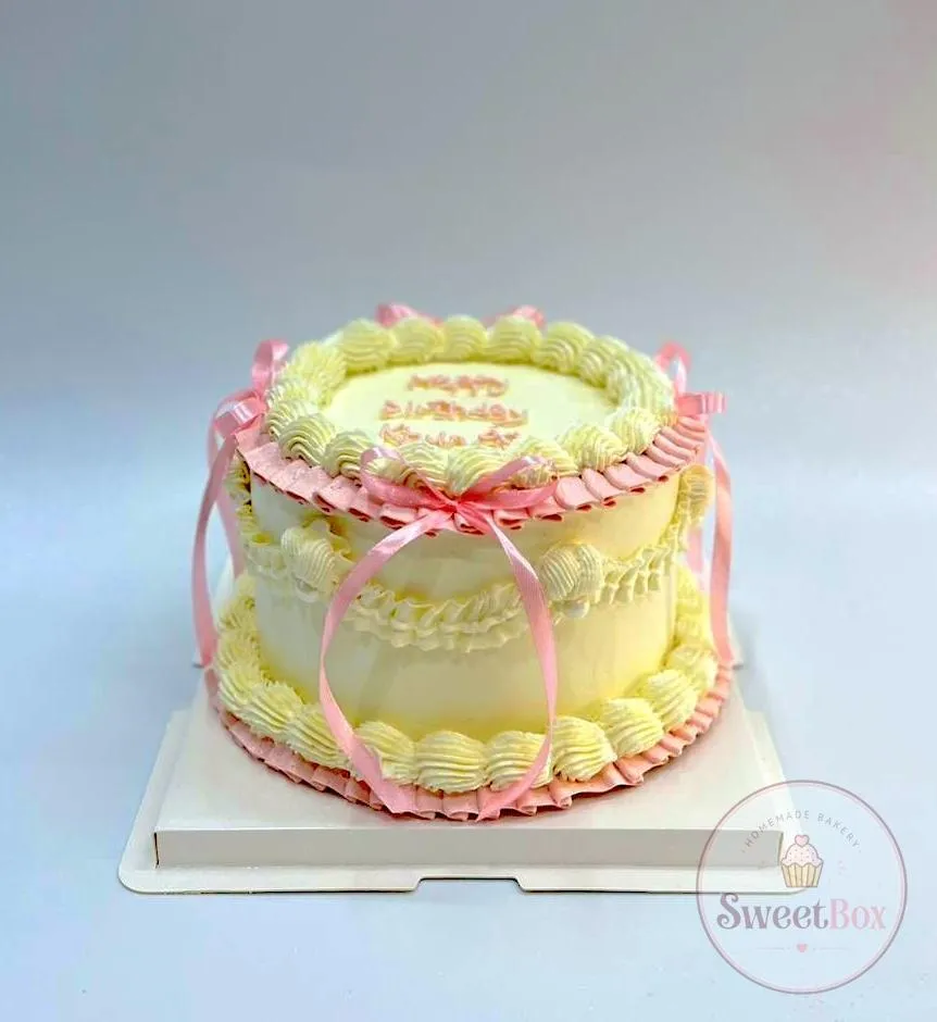 Pastel yellow vintage cake with pink piping and pink ribbon bows, with Happy Birthday on top